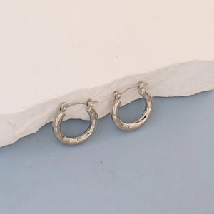 Close-up of silver oval hoop earrings with irregular geometric textured surface