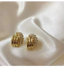 Macro shot of gold semi-hoop earrings featuring three-row cubic zirconia and metal bands