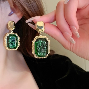 Macro detail of gold vintage earrings with large textured green rectangular gemstones