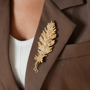 Close-up of golden feather brooch with diamonds on dark brown blazer lapel
