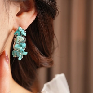 Irregular green turquoise stone earrings with silver beads on a model's ear