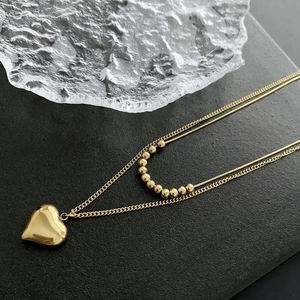 Detail of gold double-layered necklace with heart pendant and metallic beads on grey base