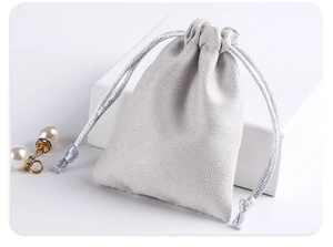 Gray microfiber velvet jewelry pouch with silver drawstring leaning on a white cube
