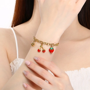 Détail d'un bracelet doré avec des breloques en émail de fraise, cerise et cadenas cœur