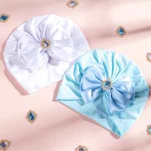 Detailed view of baby turban hats with large rhinestone bows in white and light blue
