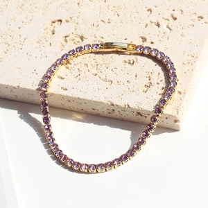 Detail of gold tennis bracelet with purple zircon stones on a beige travertine surface
