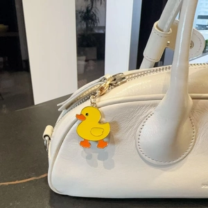 Detail of a yellow enamel duck charm with gold hook hanging on a white leather bag