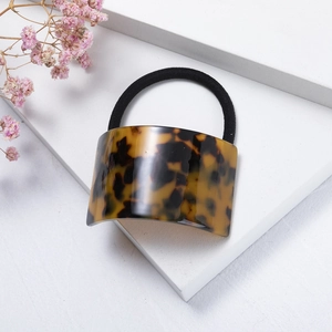 Detail of tortoiseshell acetate geometric hair tie with black elastic band on white blocks