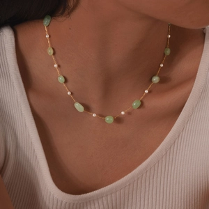 Detail of a gold necklace featuring green natural stone and white pearls on a model