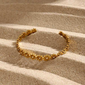 Close-up of 18k gold daisy cuff bracelet with sparkling zircon centers on sand background