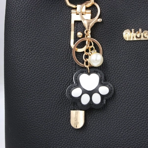 Macro detail of cat paw keychain with pearl and gold hardware on black leather bag