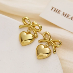 Detailed close-up of golden bow and heart drop earrings on soft silk fabric background