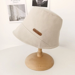 Beige cotton bucket hat with leather Hand Made tag on a wooden stand for sun protection