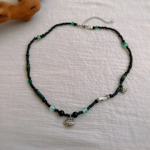 Détail macro du collier ras de cou avec perles noires, jade vert et pendentif cadenas