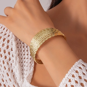 Detail of a layered golden wavy metal arm cuff bracelet worn by a model in soft lighting