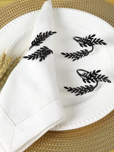 Detail of four matte black wheat leaf metal napkin rings on white cloth and gold placemat