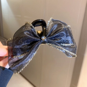 Détail de pince à cheveux noeud en tulle noir avec bordure dorée et pierre précieuse