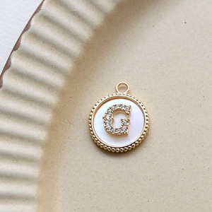 Detail of a 18k gold plated round shell pendant featuring a zircon encrusted letter G