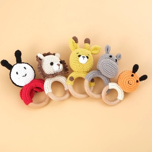 Set of five handmade crochet animal baby rattles with natural wooden rings on beige background