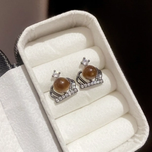 Macro shot of silver crown earrings featuring a brown pearl and sparkling zircon details