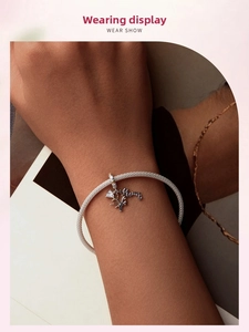 Detail showing a silver mesh bracelet with a Mom letter pendant worn on a female wrist