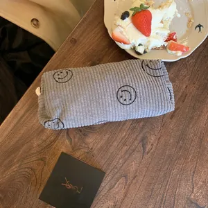 Detailed macro of grey corduroy makeup bag with black smiles on a wooden table