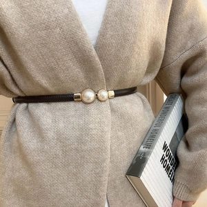 Detail view of a thin dark leather belt with a gold clasp and two large pearls on a cardigan