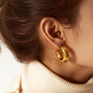Close-up of a minimalist polished gold hoop earring worn by a model in a lifestyle setting
