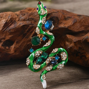 Macro shot of green and gold snake brooch with blue crystals on dark wood surface