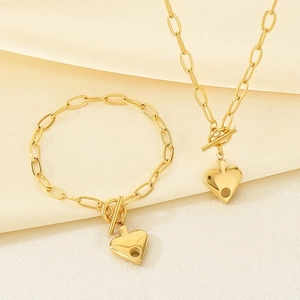 Macro detail of 18K gold-plated paperclip chain and heart charm with spade cutout on silk