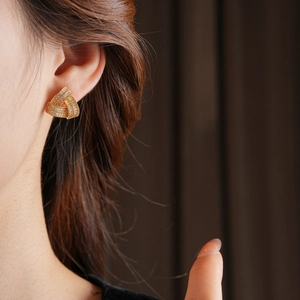 Gros plan de boucles d'oreilles triangle tressé doré avec zircons sur un mannequin