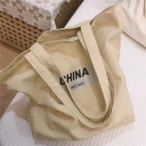 Détail d'un grand sac cabas en toile beige avec imprimés lettres noires sur un lit blanc