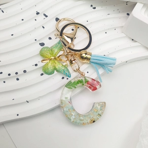 Macro detail of resin letter C keychain with green dried flowers and gold foil accents
