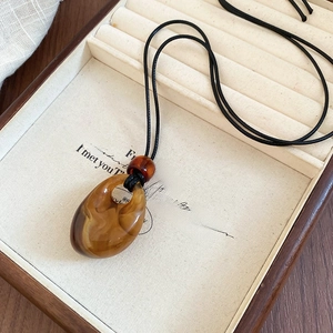 Close-up of a vintage brown resin waterdrop pendant on a black wax cord in a wooden tray