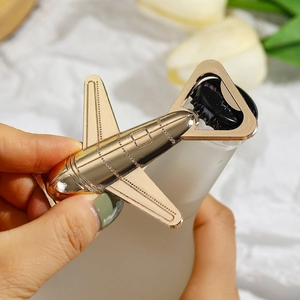 Airplane-shaped gold metal bottle opener used to open a glass bottle cap in close-up shot