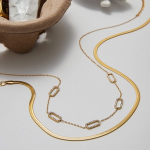 Close-up of gold layered necklace featuring a snake chain and pavé zircon bar elements