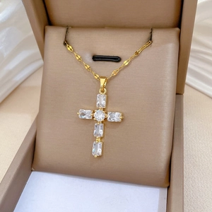 Gros plan d'un collier croix en titane doré serti de zircons dans son écrin cadeau