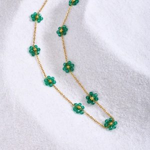 Macro detail of gold cross chain necklace featuring emerald green beaded flower motifs