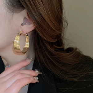 Close-up of model wearing chunky layered gold hoop earrings with metallic luster finish