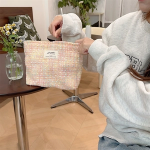 Close-up of pink tweed makeup bag with woven fabric texture and white brand label