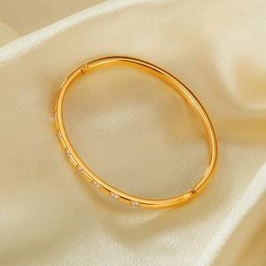 Detail of a gold-plated stainless steel hinge bracelet with sparkling zircon on champagne satin