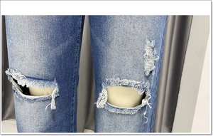 Detailopname van een blauwe jeans met grote scheuren bij de knie en gerafelde denim textuur