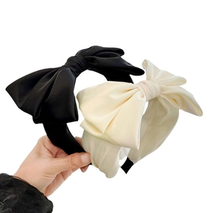 Elegant bow headband in black and creamy white silk fabric shown in a stylish hand-held view