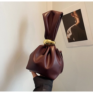 Detail of burgundy drawstring bucket bag featuring a sleek gold circular metal handle