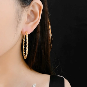 Close-up of a model wearing large gold hoop earrings with a textured geometric surface
