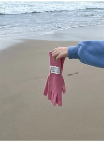 Close-up of pink wool knitted gloves with a white brand label against a beach background