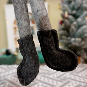 Close-up of Christmas gnome felt legs and black boots with festive tree background