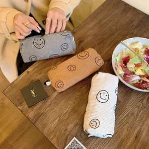 Close-up of corduroy makeup bags in grey, brown and white with embroidered smiley face