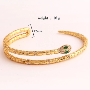 Detail view of gold snake-shaped bangle featuring green gemstone eyes and 12mm width