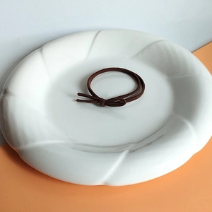 Detailed texture of a brown high-elasticity hair tie with a knot detail on a ceramic dish